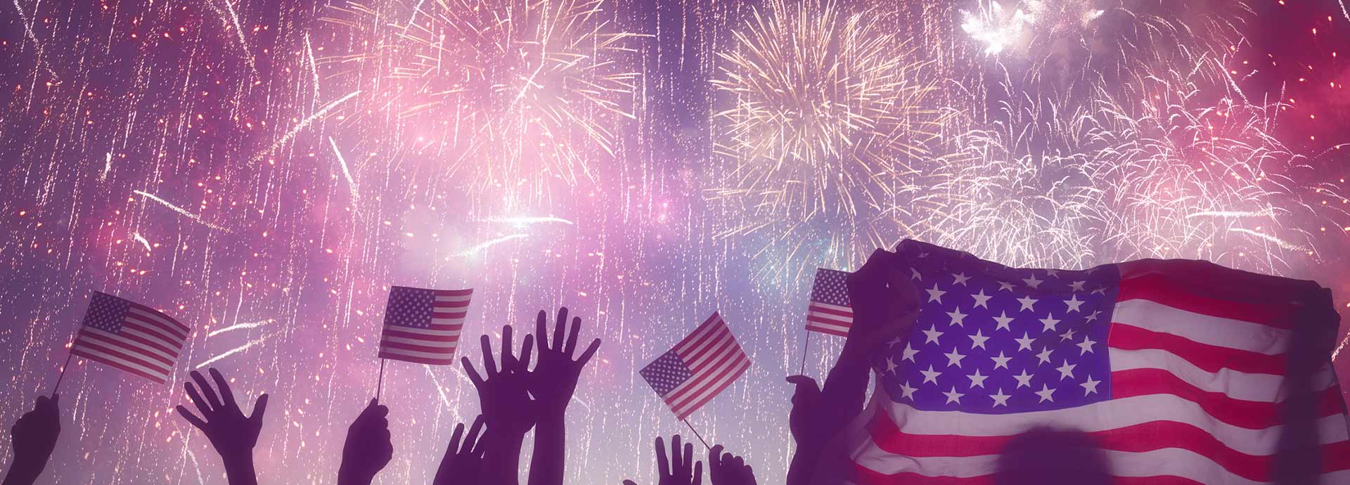 Image of people holding United States flags with fireworks in the sky