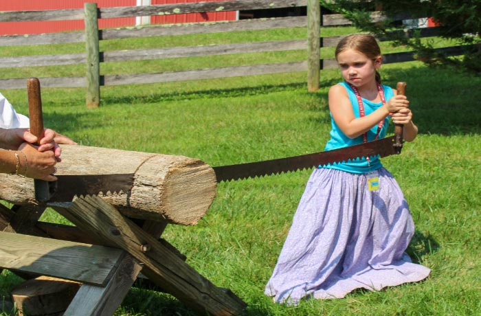 Image of a small girl helping to saw a log