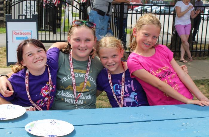 Image of four young girls seated at a table with their arms around each other