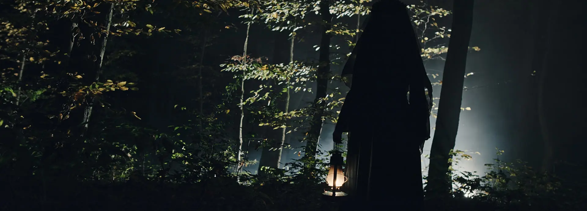 Image of a ghostly figure holding a lit lantern in the woods